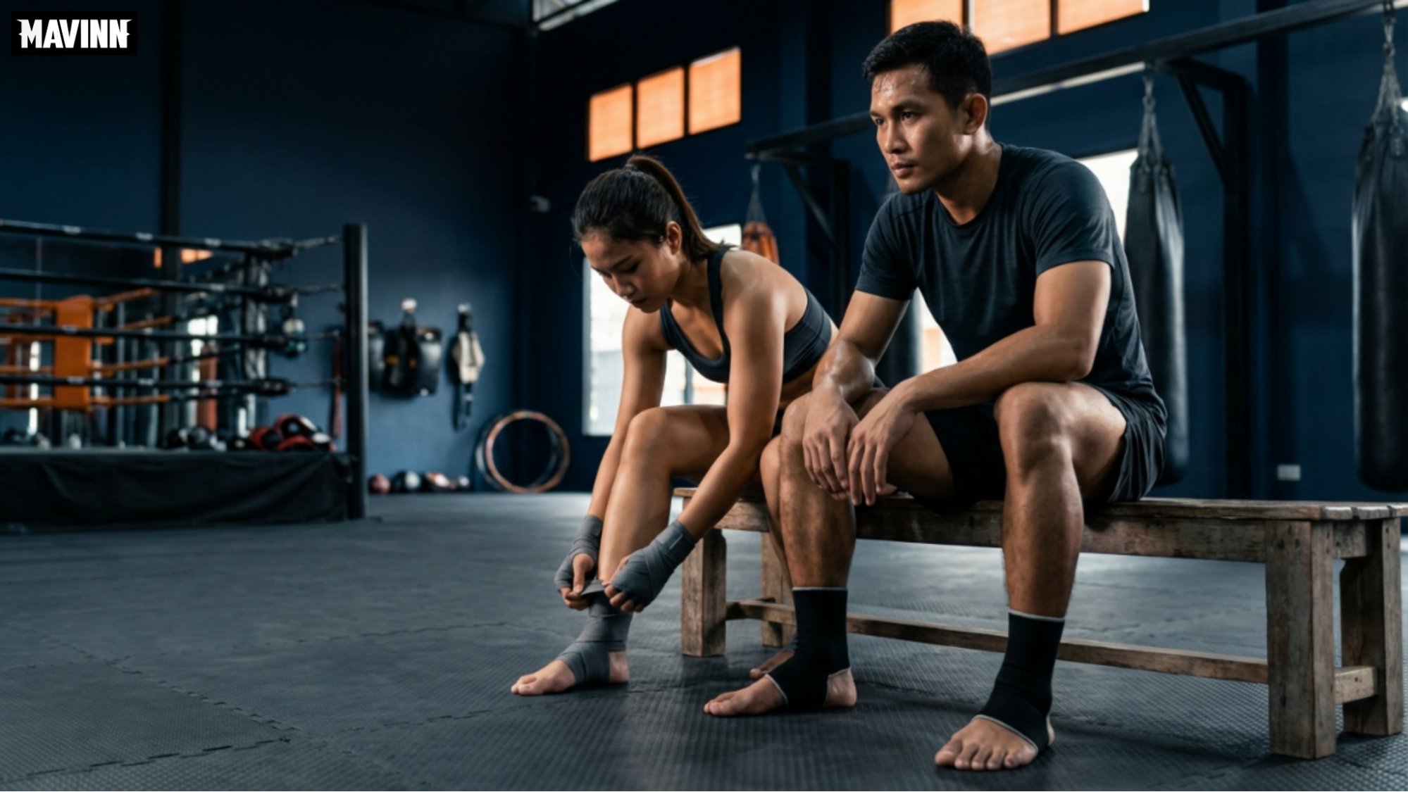 Female fighter adjusting her Muay Thai foot wrap next to a male partner on a gym bench