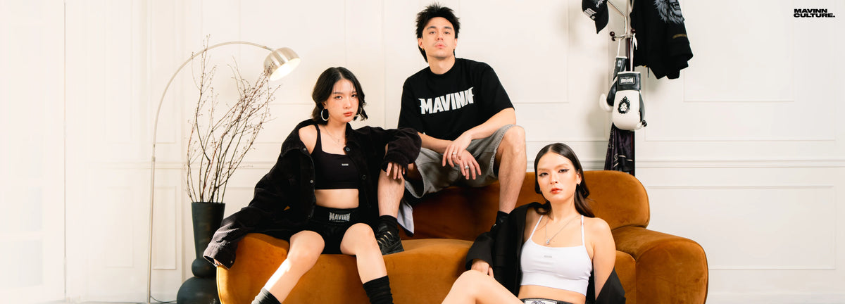 Three models in MAVINN streetwear: black logo tee, sports bras and Muay Thai shorts, styled with boxing gloves in a living room